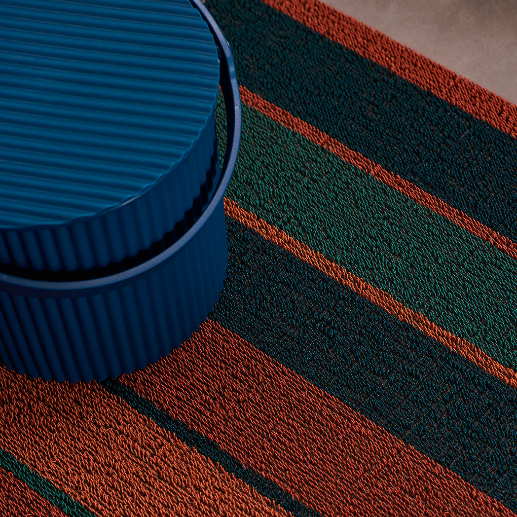 Chilewich striped woven mat with textured terrastrand yarn surface, featuring modern linear design and durable finish.